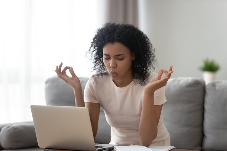 A stressed woman tries to meditate in front of her laptop.
