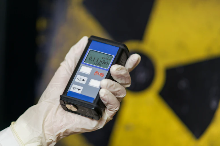 Una mano enguantada sostiene un contador Geiger delante del logotipo nuclear.