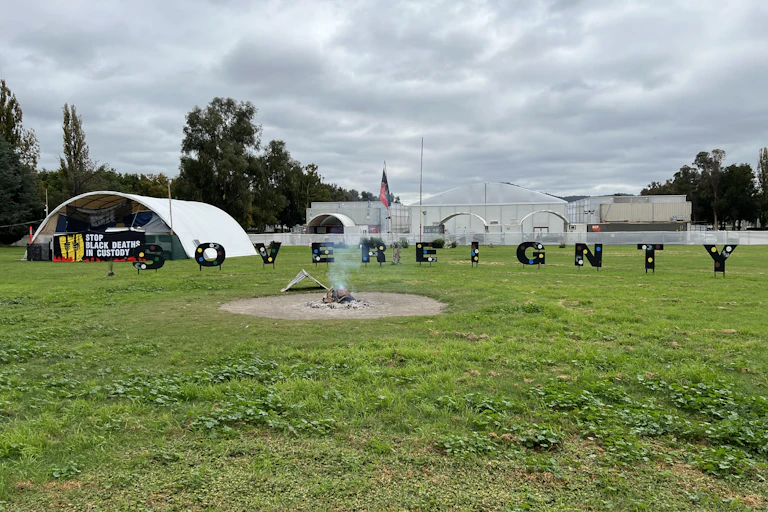 A fire burns in front of a sign saying 'sovereignty' and tents of the Aboriginal Tent Embassy.