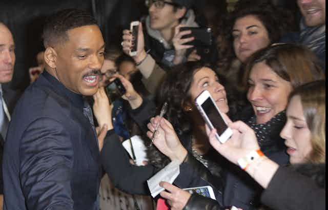 Will Smith stands in front of adoring fans with microphones, pens and phones