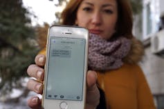 a woman with dark hair holds up a smartphone