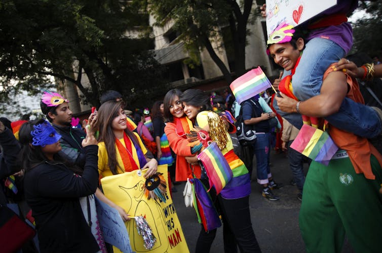 Indians from the LGBTQ community in colorful dresses walking in a Queer Pride parade, while holding the six-color pride flag.