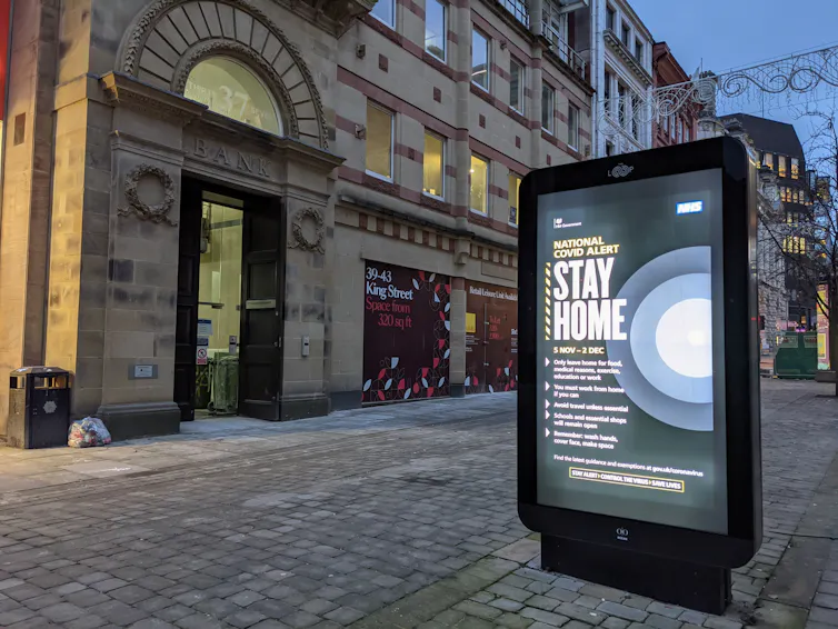 An advertising screen on a Manchester street showing public health guidance to Stay Home.