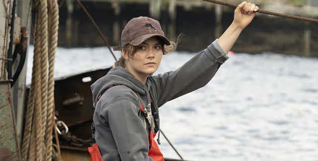 A young woman in a cap on a boat holds a rope line.
