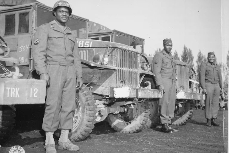 Three black soldiers are standing in front of several military trucks.t