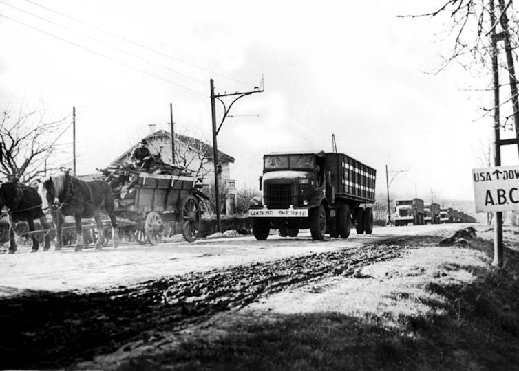 A convoy of trucks carrying military supplies is seen on a narrow road.