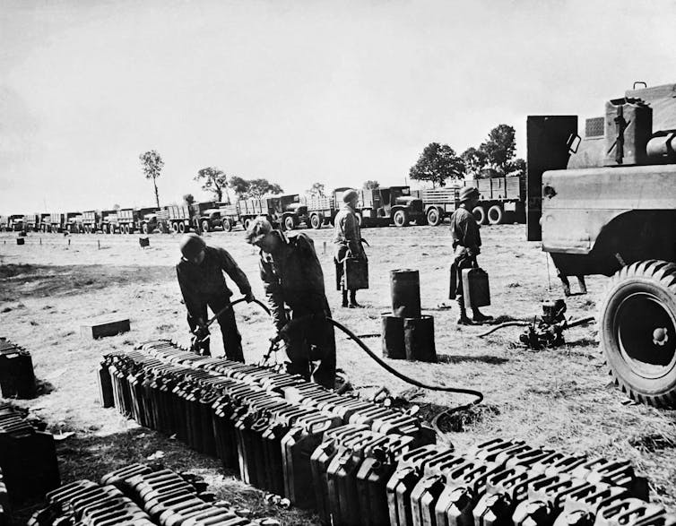 Se ven soldados negros llenando tanques de gasolina para docenas de camiones utilizados para transportar suministros militares.