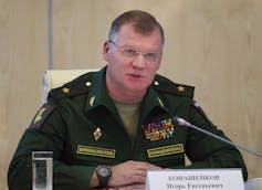 A man in a military uniform wearing glasses speaks into a microphone.