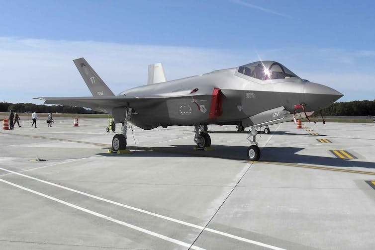 A fighter jet sits on an airport tarmac on a sunny day.