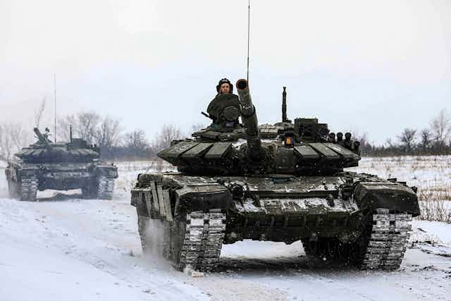 two tanks travel along a snow-covered road through an open field