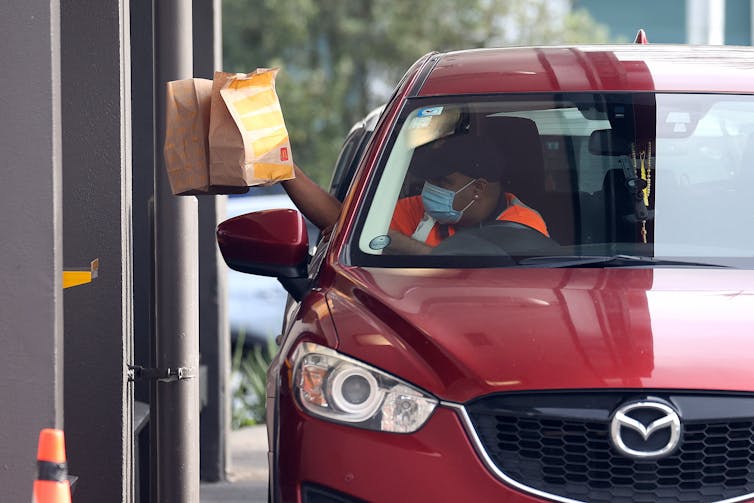 Man holds two packets of takeaway food while siting in his car.