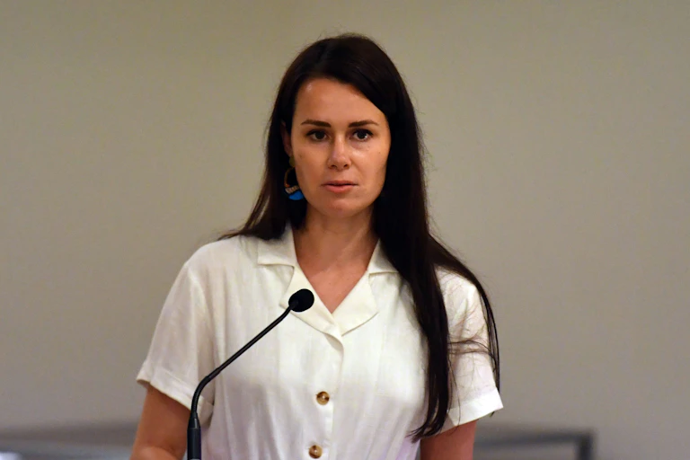 A woman standing by a microphone, looking serious.