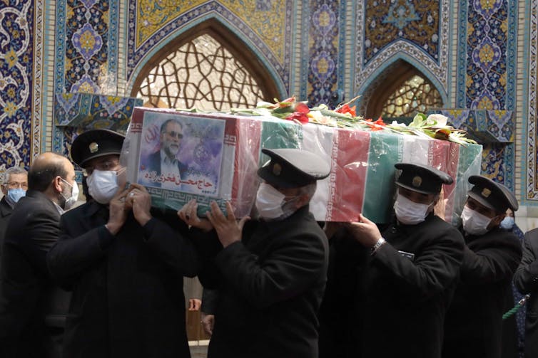 A coffin draped in the Iranian flag being carried through a shrine by military men.