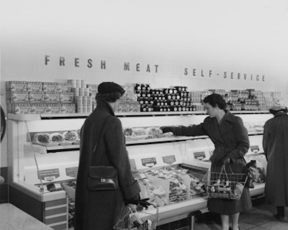 Women holding shopping baskets in front of a counter with a sign saying fresh meat self-service.