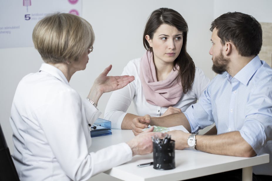 Couple in their 20s or 30s look at each other with concern during a consultation with a doctor.