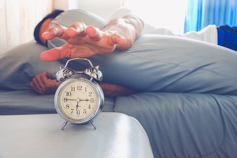 Man in bed reaching to switch off his alarm clock