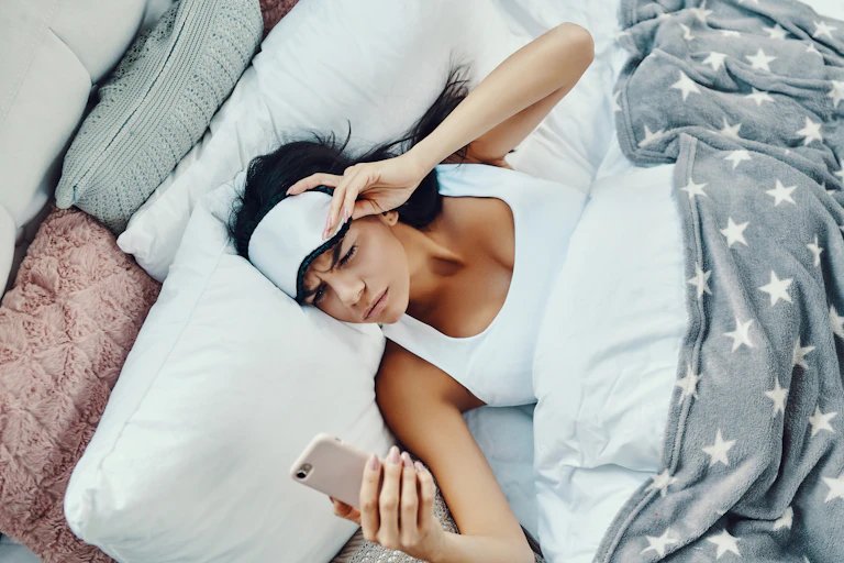 Photo d’une jeune femme qui semble avoir du mal à se réveiller et regarde son téléphone.
