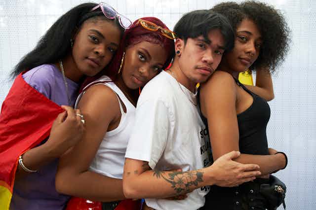Four young trans people of color embracing each other front to back