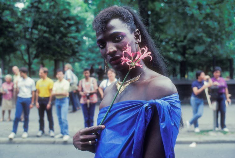Black trans woman of color holding flower at a Pride March event.