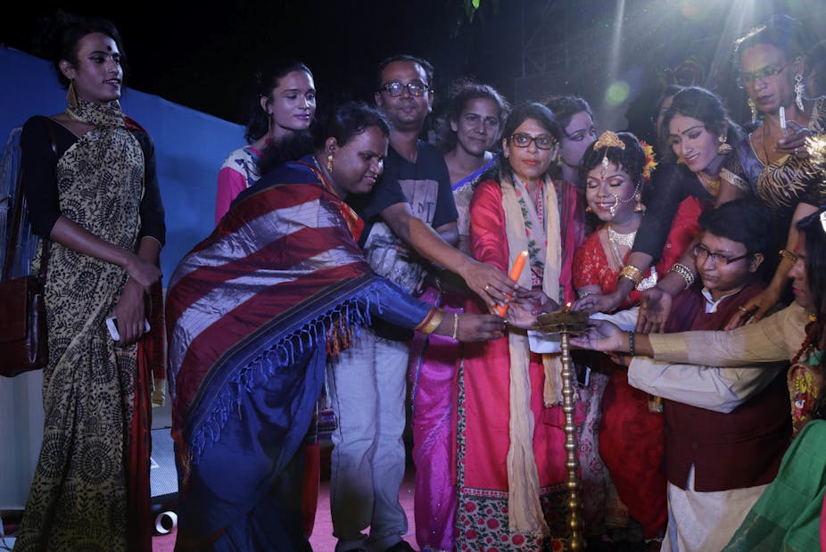 Several trans women dressed in saris lighting a tall brass lamp in Kolkata, India.