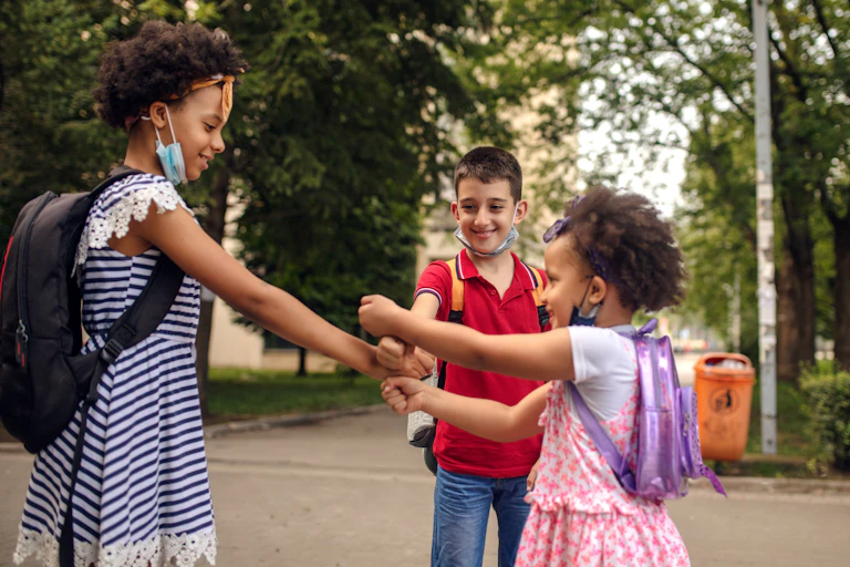 Three children wearing masks play "hot potato" with one another outside.