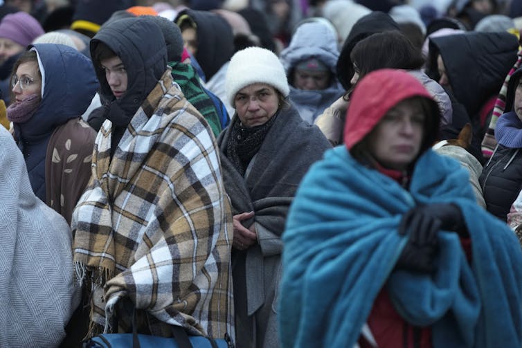 People in shawls and blankets stand in a crowd.