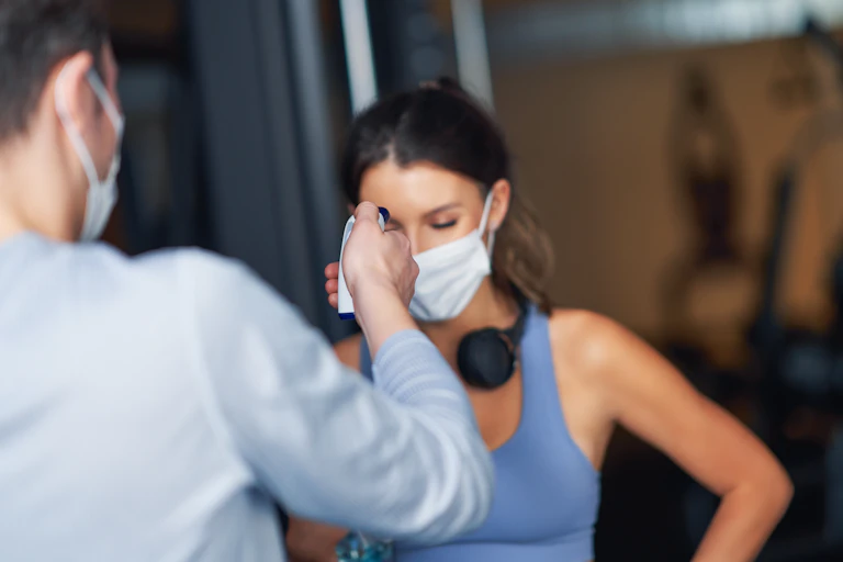 Une jeune femme en tenue de sport, yeux baissés, se fait prendre la température en salle