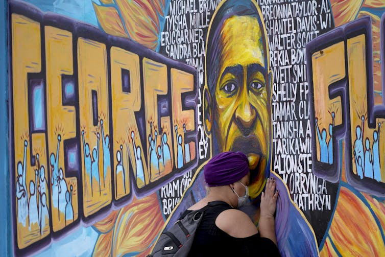 A woman presses her face up against a mural of George Floyd.