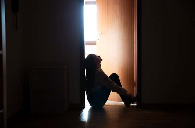 Backlit teenager sitting in a dark indoor doorway in contemplation.