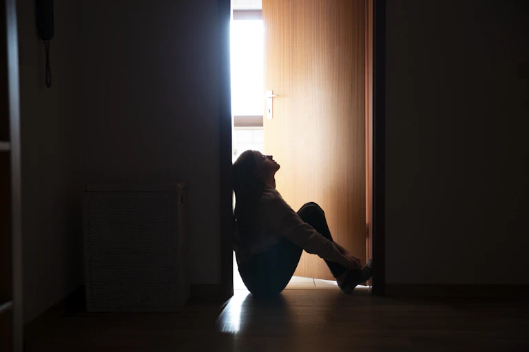 Backlit teenager sitting in a dark indoor doorway in contemplation.