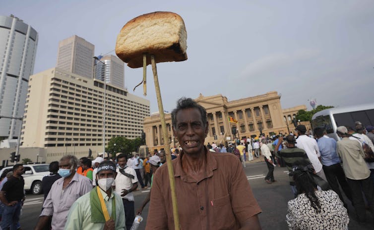 A man holds a stick with a loaf of bread at the end amid a crowd of protesters