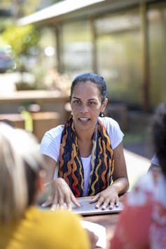 A person sits in the sun, having a discussion with other students.