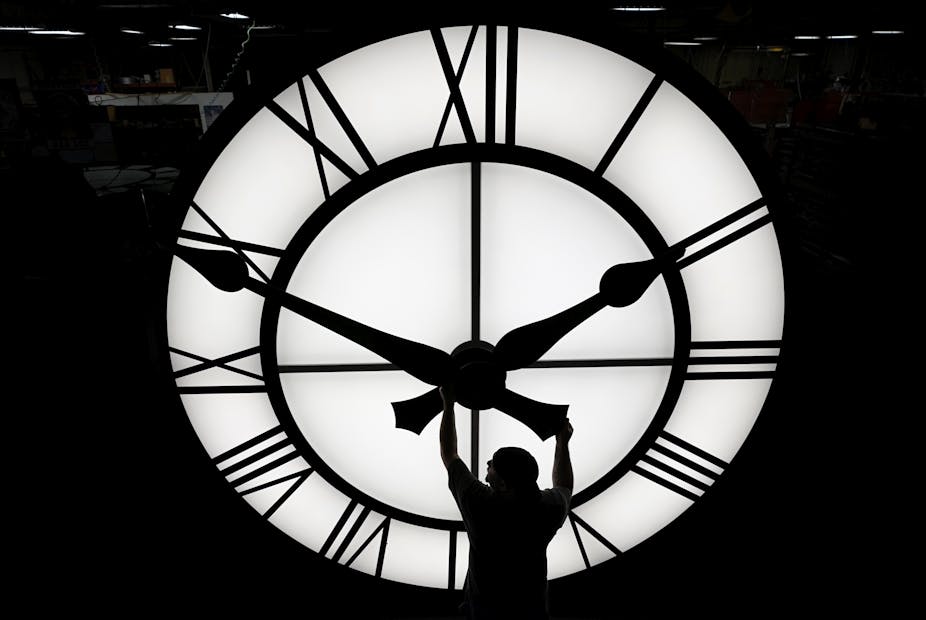 man adjusts time of giant clock in black and white