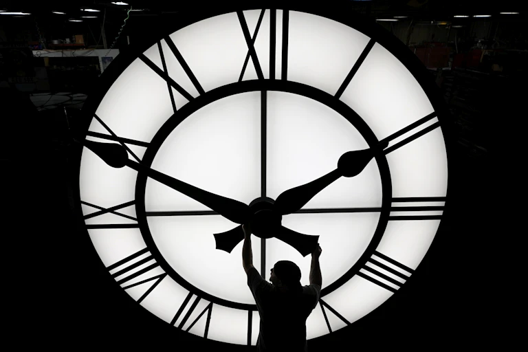 man adjusts time of giant clock in black and white