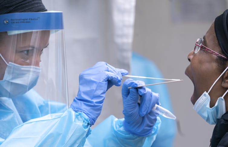 A health-care worker in PPE about to swab a patient's throat