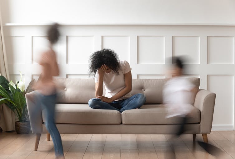 Image of a mother feeling stressed while kids play around her.