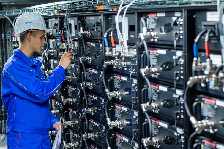 An engineer in blue overalls inspects a row of power storage units.