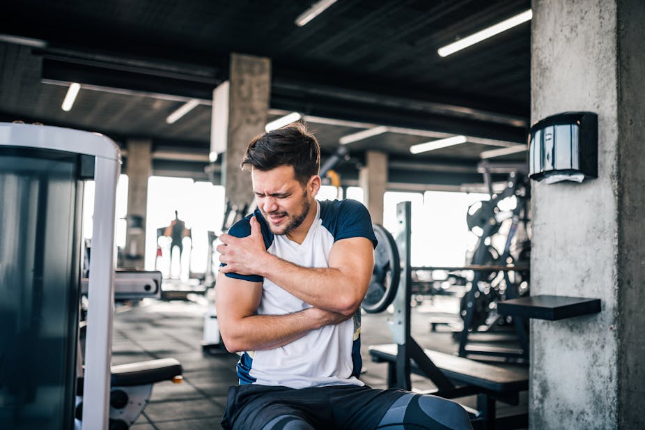 Man in gym holds his upper arm in pain.