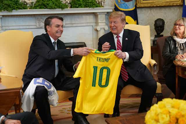 Two men holding a yellow shirt with Trump written on it.
