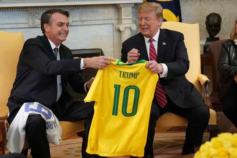 Two men holding a yellow shirt with Trump written on it.