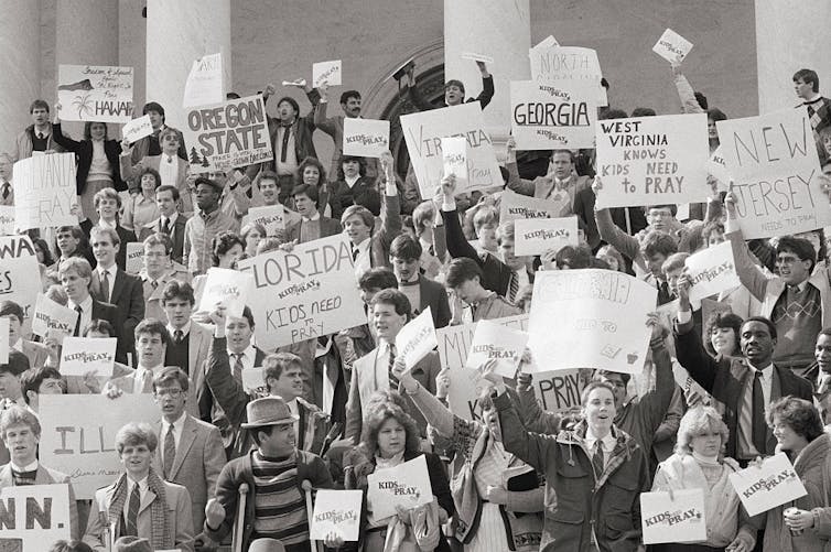 A black and white photo shows people protesting on the steps of a building with white columns.