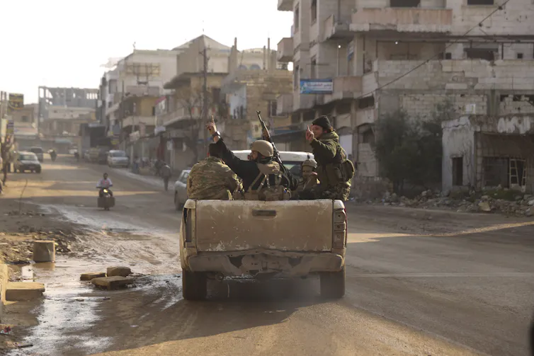 armed men drive in an armoured vehicle through a rural village