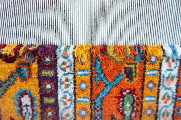 A colourful carpet being woven on a loom