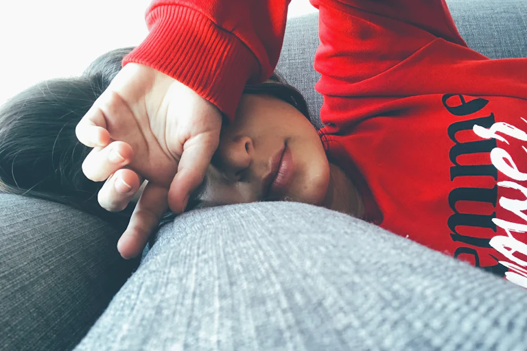 Woman lying on sofa covering eyes with back of hand