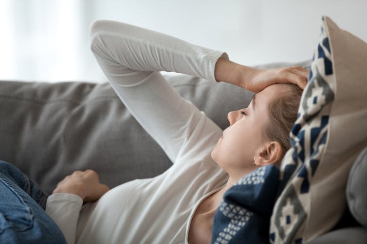 Fatigued woman lying on sofa clutching her head