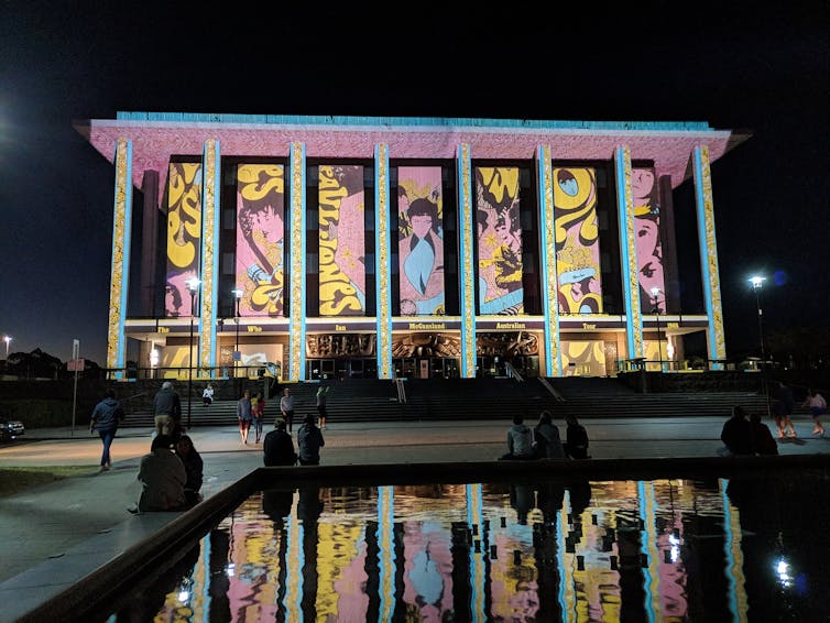 A light projection across the National Library walls at night, with people looking on