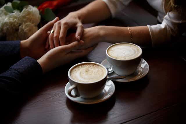 Two sets of entwined hands next to cups of coffee