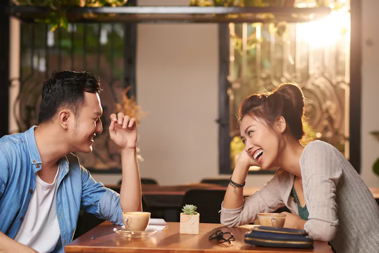 Couple on a first date laughing at the table over coffees.