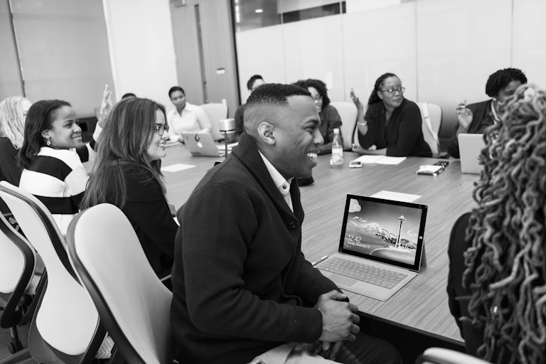 A group of people sitting at a large table with laptops and papers before them