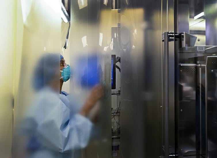 Blurred view of a health-care worker behind a plastic curtain, wearing PPE